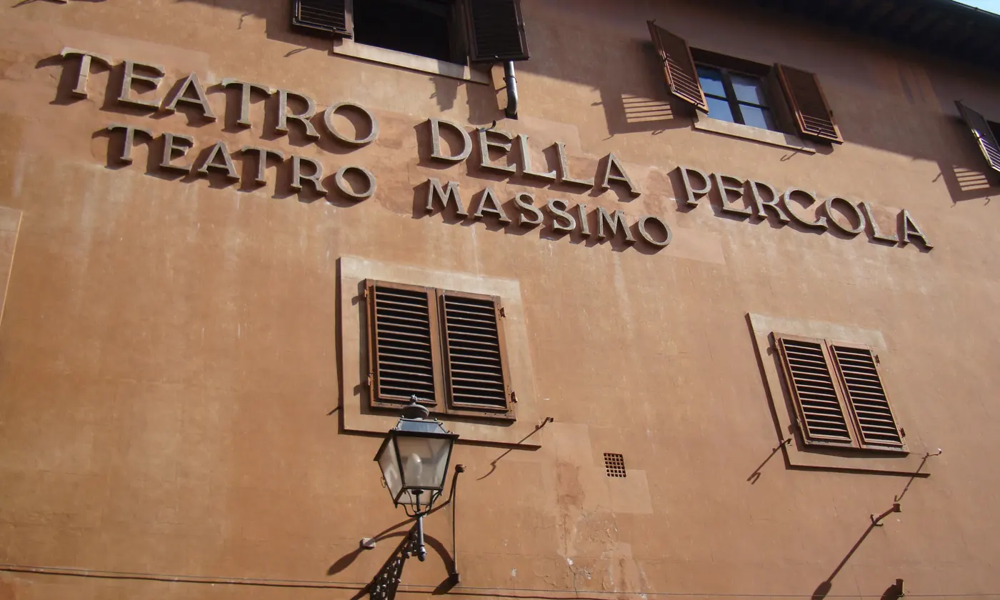 Die ockerfarbene Wand des Teatro della Pergola in Florenz, mit dem Namen in erhabenen Buchstaben, hölzernen Fensterläden und einer Straßenlaterne