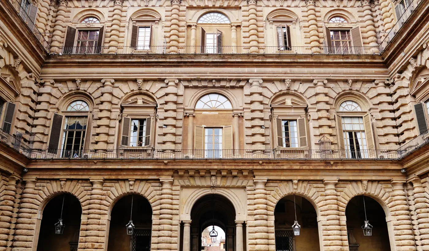 Ein steinerner Innenhof des Palazzo Pitti in Florenz, dessen wuchtige, grob behauene Mauern von Bögen und Fensterreihen durchbrochen werden