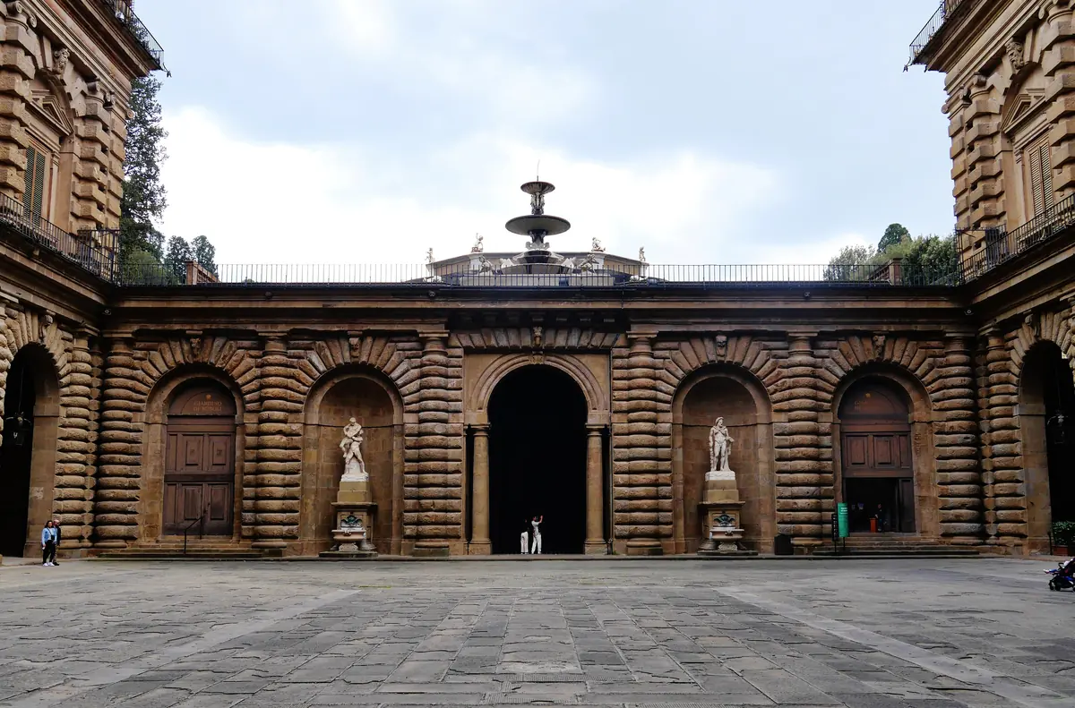 Vysoké rustikální nádvoří Palazzo Pitti ve Florencii s fontánou v zadní části pod širokým obloukem