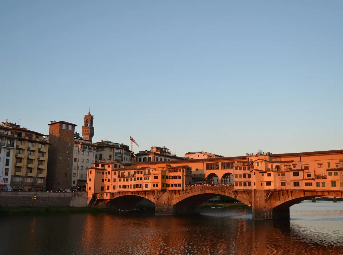 Ponte Vecchio ved solnedgang i Firenze, med butikkerne på broen oplyst i orange over Arno